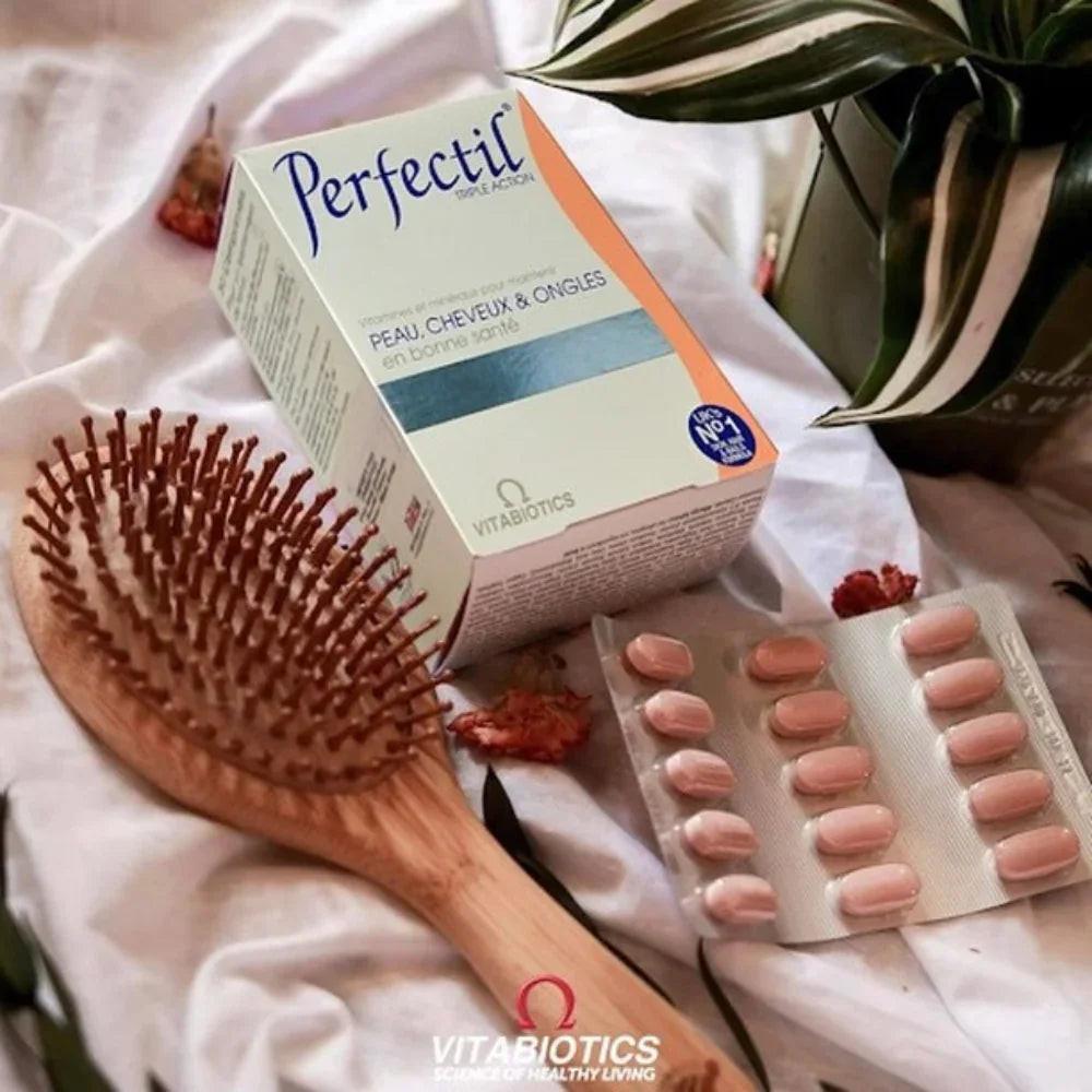 Boite de perfectil sur un tissu blanc, avec une brosse cheveux et une plante