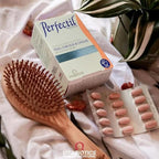 Boite de perfectil sur un tissu blanc, avec une brosse cheveux et une plante